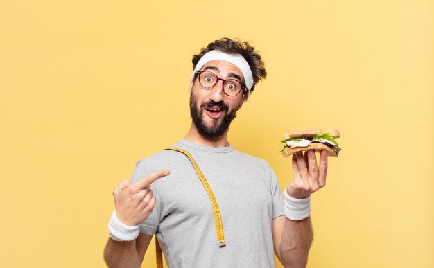 Jeune athlète barbu fou a surpris l'expression et tenant un sandwich