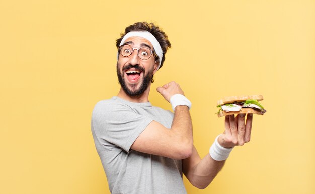 Jeune athlète barbu fou a surpris l'expression et tenant un sandwich