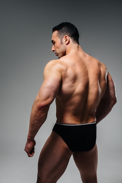 Un jeune athlète bodybuilder pose en studio dos nu