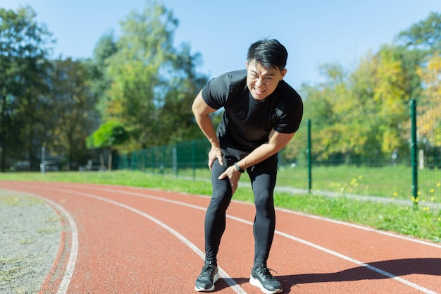 Jeune athlète de coureur asiatique avec un homme souffrant de douleurs musculaires massant une blessure traumatique d'étirement tout en faisant du jogging à