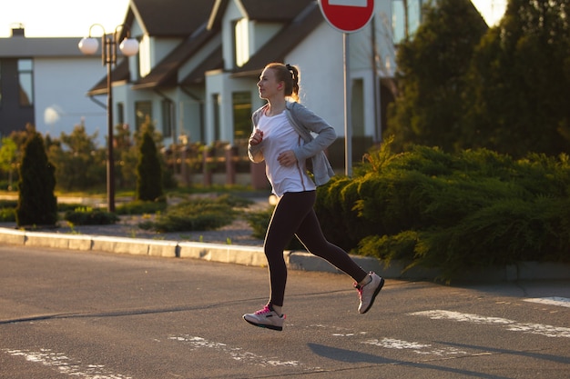 Jeune athlète de coureur féminin fait du jogging dans la rue de la ville au soleil Belle femme de race blanche