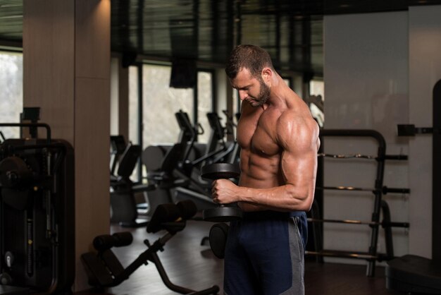 Jeune athlète dans la salle de gym effectuant des boucles de biceps avec des haltères