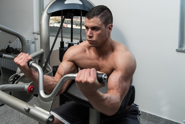 Jeune athlète faisant des exercices de poids lourds pour les biceps sur la machine