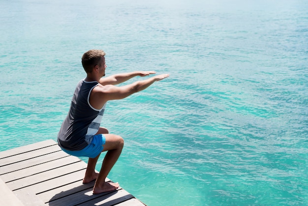 Jeune athlète faisant des squats sur le quai de la mer. Mode de vie d'été sain.