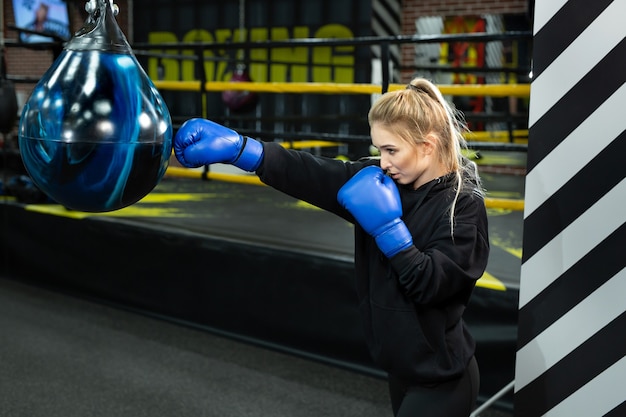 Jeune athlète en gants de boxe bleus frappe une poire dans le ring