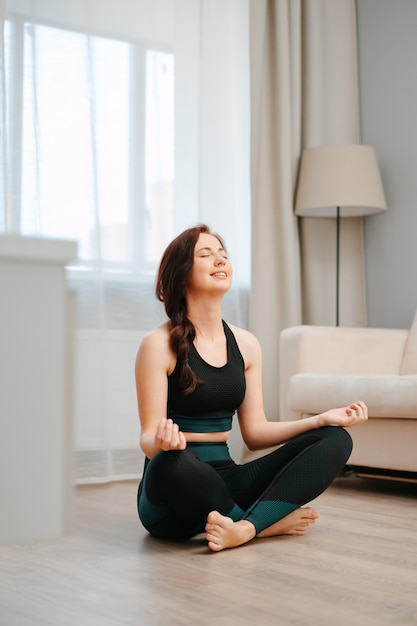 Jeune athlète heureux dans la position du lotus est assis sur le sol de la maison faisant du yoga