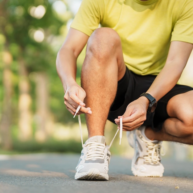 Jeune athlète homme attachant des chaussures de course dans le parc coureur masculin en plein air prêt à faire du jogging sur la route à l'extérieur de l'Asie Marche de remise en forme et exercice sur le sentier dans les concepts de bien-être et de sport du matin