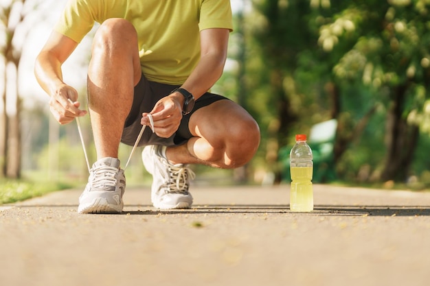 Jeune athlète homme attachant des chaussures de course avec de l'eau Energy Drink coureur masculin prêt pour le jogging à l'extérieur de l'Asie Fitness marche et exercice dans le parc matin bien-être bien-être et concepts sportifs