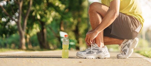 Jeune athlète homme attachant des chaussures de course avec de l'eau Energy Drink coureur masculin prêt pour le jogging à l'extérieur de l'Asie Fitness marche et exercice dans le parc matin bien-être bien-être et concepts sportifs