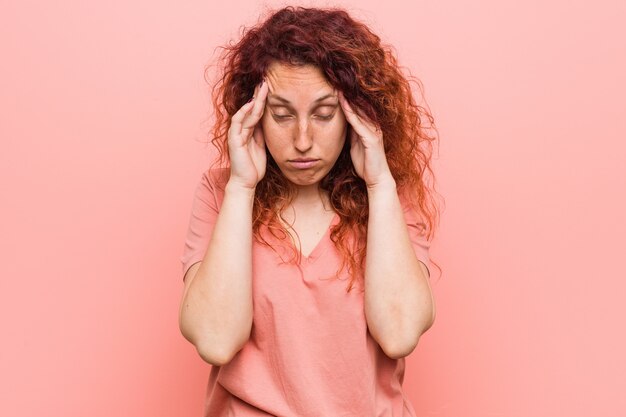 Jeune et authentique femme rousse touchant les tempes et ayant mal à la tête