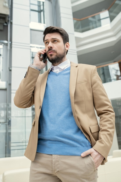 Jeune avocat sérieux et confiant en costume beige marchant dans le hall et appelant le client par téléphone