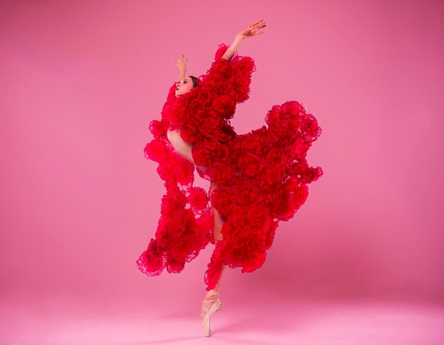 une jeune ballerine dans un studio photo dans une robe de cape faite de fleurs de rose montre des mouvements de ballet