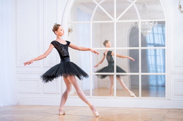 Jeune Ballerine Dans Un Tutu Noir Se Dresse Dans Une Pose Gracieuse Sur Des Pointes Dans Une Grande Salle Lumineuse Devant Un Miroir.