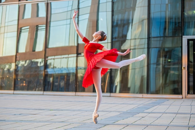 Une jeune ballerine dans un tutu rouge vif danse sur fond de paysage urbain