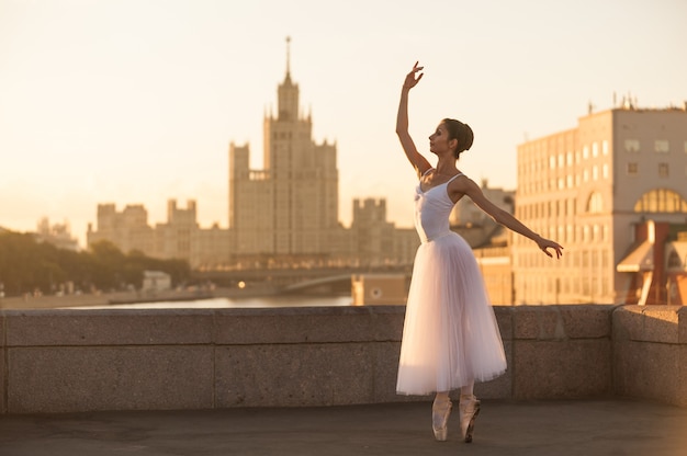 Jeune ballerine dansant le matin contre les silhouettes des bâtiments de la ville