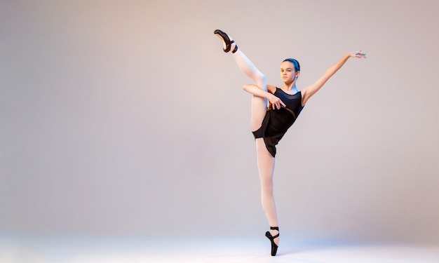 Une jeune ballerine en maillot de bain noir et pointes danse sur un fond clair.