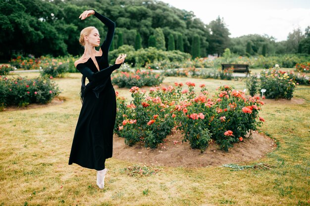 Jeune ballerine en robe noire posant et montrant des poses de ballet dans le parc d'été.