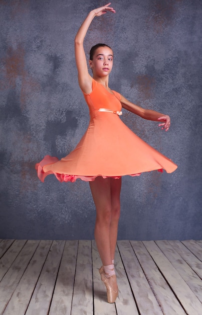 Photo la jeune ballerine en robe orange danse en studio sur fond gris