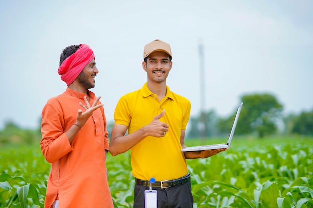 Jeune banquier ou agronome indien montrant des détails aux agriculteurs dans un ordinateur portable dans le domaine de l'agriculture.