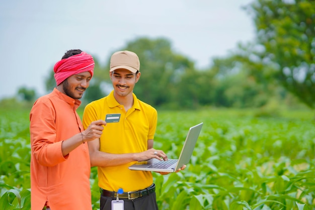 Jeune banquier ou agronome indien montrant des détails aux agriculteurs dans un ordinateur portable dans le domaine de l'agriculture.