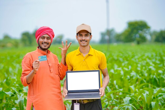 Jeune banquier ou agronome indien montrant un écran d'ordinateur portable avec un agriculteur dans un domaine agricole.