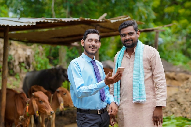 Jeune banquier indien montrant quelques détails à l'agriculteur dans un smartphone.