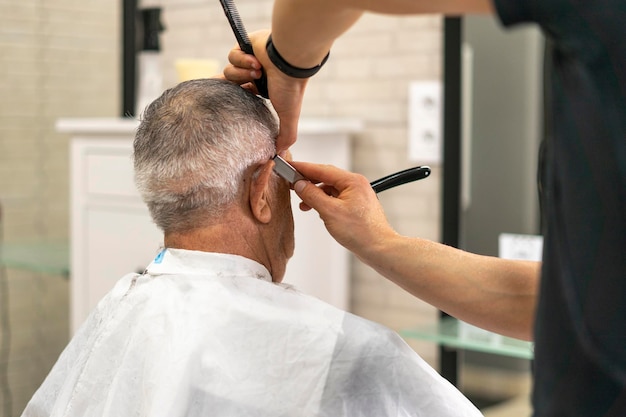 Jeune barbier utilisant le rasoir pour terminer la coupe de cheveux d'un vieil homme