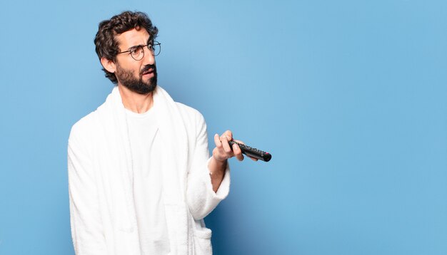 Jeune barbu fou portant un peignoir avec une télécommande