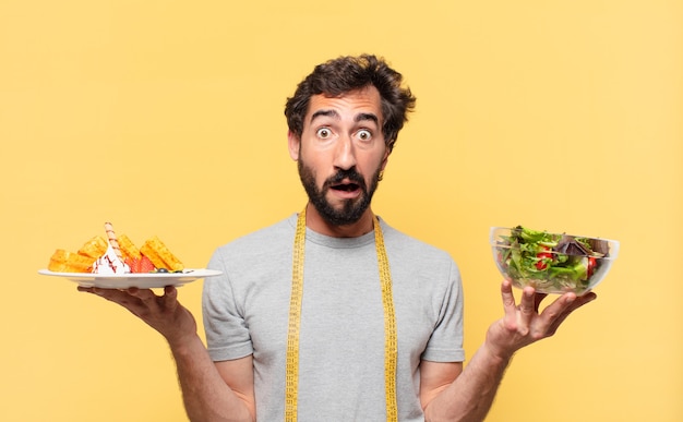 Jeune barbu fou suivant un régime doutant ou d'expression incertaine et tenant une salade et des gaufres