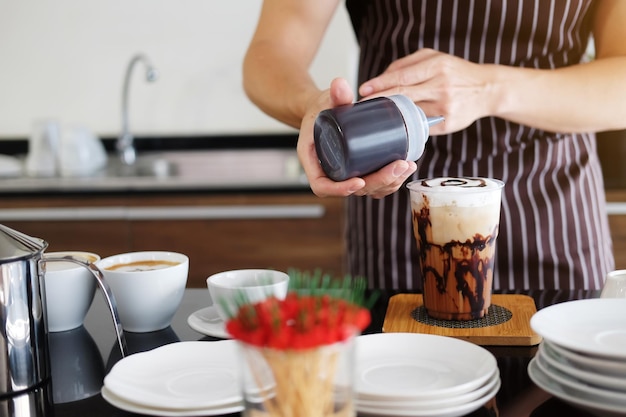 Jeune barista asiatique versant de l'art du chocolat frais dans un verre en plastique de café glacé Cappuccino