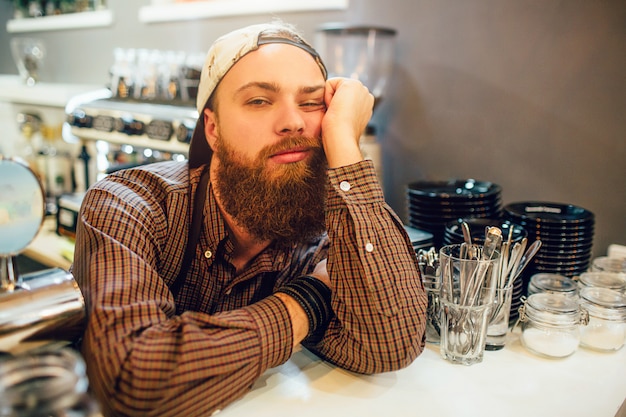 Jeune barista s'ennuie se penche sur la table et regarde la caméra