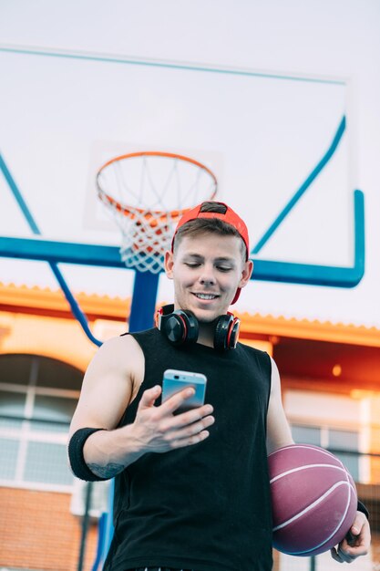 jeune basketteur avec un ballon regarde son téléphone portable et sourit en faisant une pause