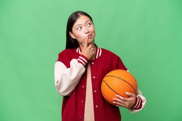 Jeune basketteur femme asiatique sur fond isolé ayant des doutes en levant les yeux