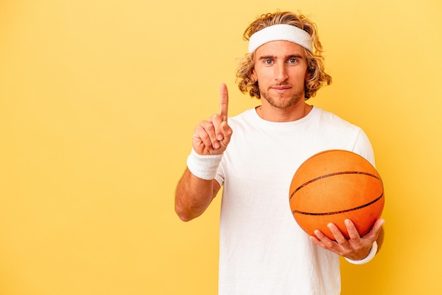 Jeune basketteur homme caucasien isolé sur fond jaune montrant le numéro un avec le doigt.