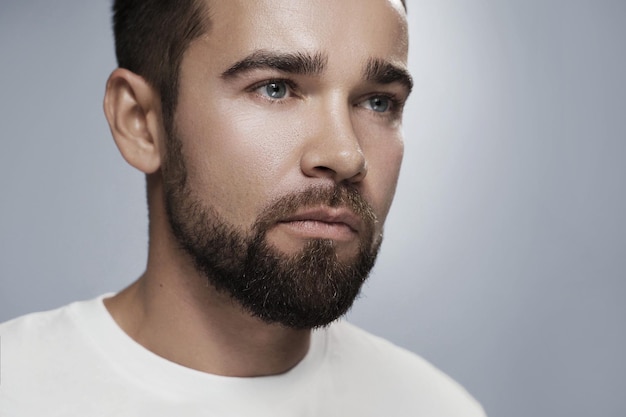 Jeune et beau barbu avec une peau propre sur fond gris