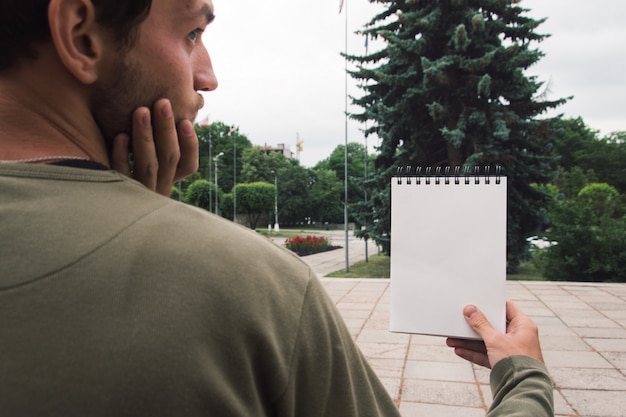 Photo jeune beau barbu tenant un bloc-notes en regardant une liste vide dans le parc