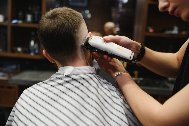 Jeune beau coiffeur faisant la coupe de cheveux de bel homme barbu en salon de coiffure