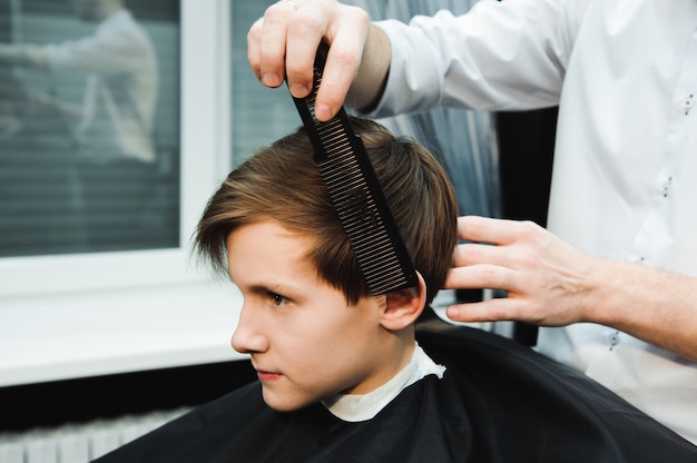 Jeune beau coiffeur faisant la coupe de cheveux de garçon mignon en salon de coiffure.