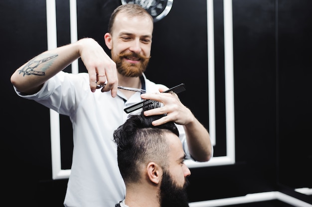 Jeune beau coiffeur faisant la coupe de cheveux d'un homme séduisant dans un salon de coiffure.