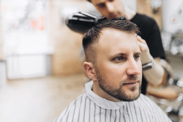 Jeune beau coiffeur faisant la coupe de cheveux d'un homme séduisant dans un salon de coiffure