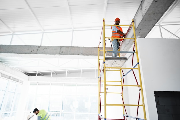 Jeune beau constructeur s'élevant sur l'échafaudage au chantier de construction