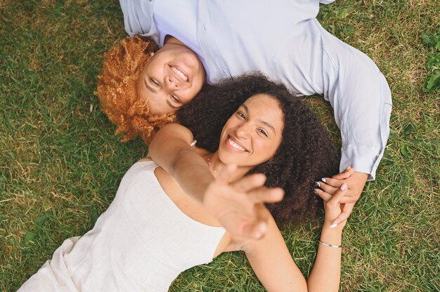 Jeune beau couple afro-américain de lesbiennes heureux allongé sur l'herbe en riant en tendant les mains