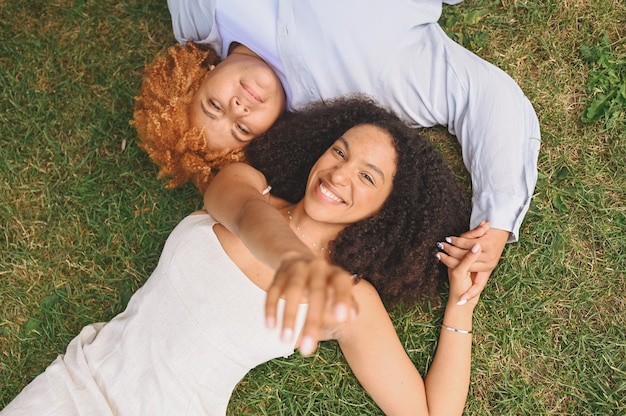 Jeune beau couple afro-américain de lesbiennes heureux allongé sur l'herbe en riant en tendant les mains