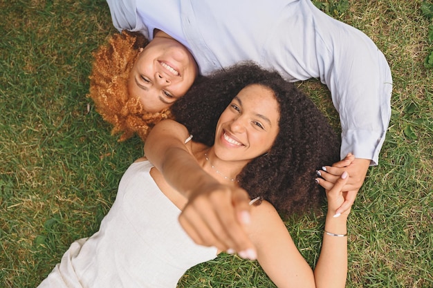Jeune beau couple afro-américain de lesbiennes heureux allongé sur l'herbe en riant en tendant les mains