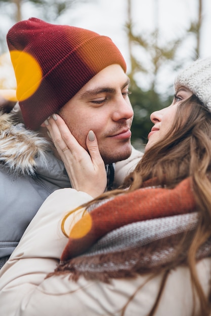 Jeune beau couple amoureux câlins et bisous dans une forêt de conifères d'hiver. Un parc avec des arbres de Noël en arrière-plan. Ambiance de Noël. Teinture.