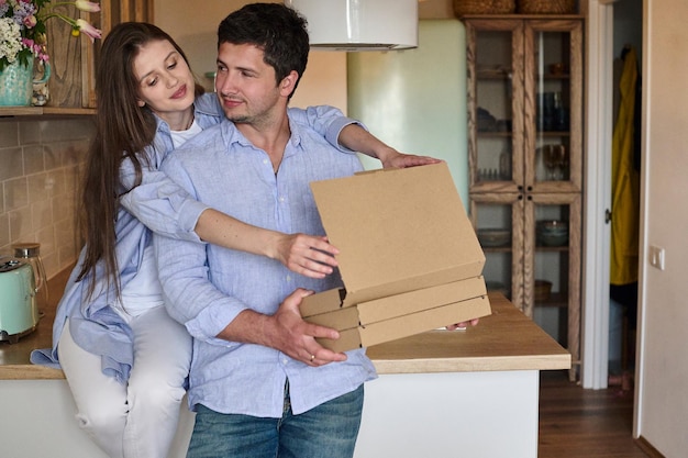 Jeune beau couple avec des boîtes à pizza dans les mains dans la cuisine Concept de livraison rapide