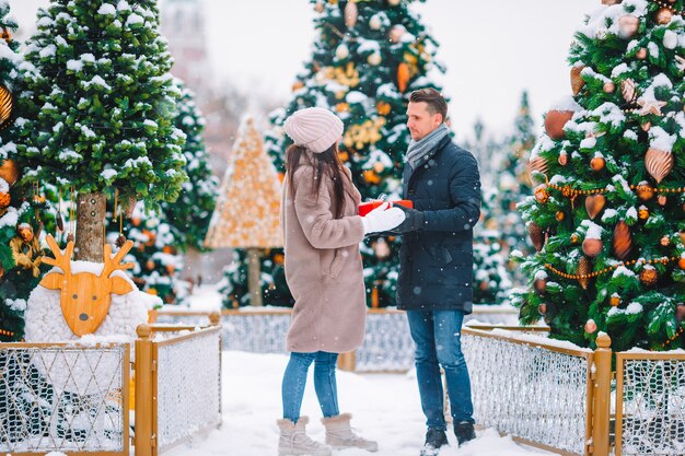 Jeune beau couple célébrant Noël dans la rue de la ville et se donnant des cadeaux