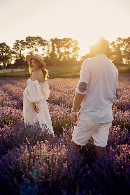 Jeune beau couple enceinte marchant sur un champ de lavande au coucher du soleil Concept de famille heureuse