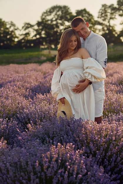Jeune beau couple enceinte marchant sur un champ de lavande au coucher du soleil Concept de famille heureuse