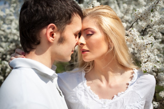 Jeune beau couple femme et homme s'embrassant sur fond d'arbres joyeux en fleurs sur une journée ensoleillée claire